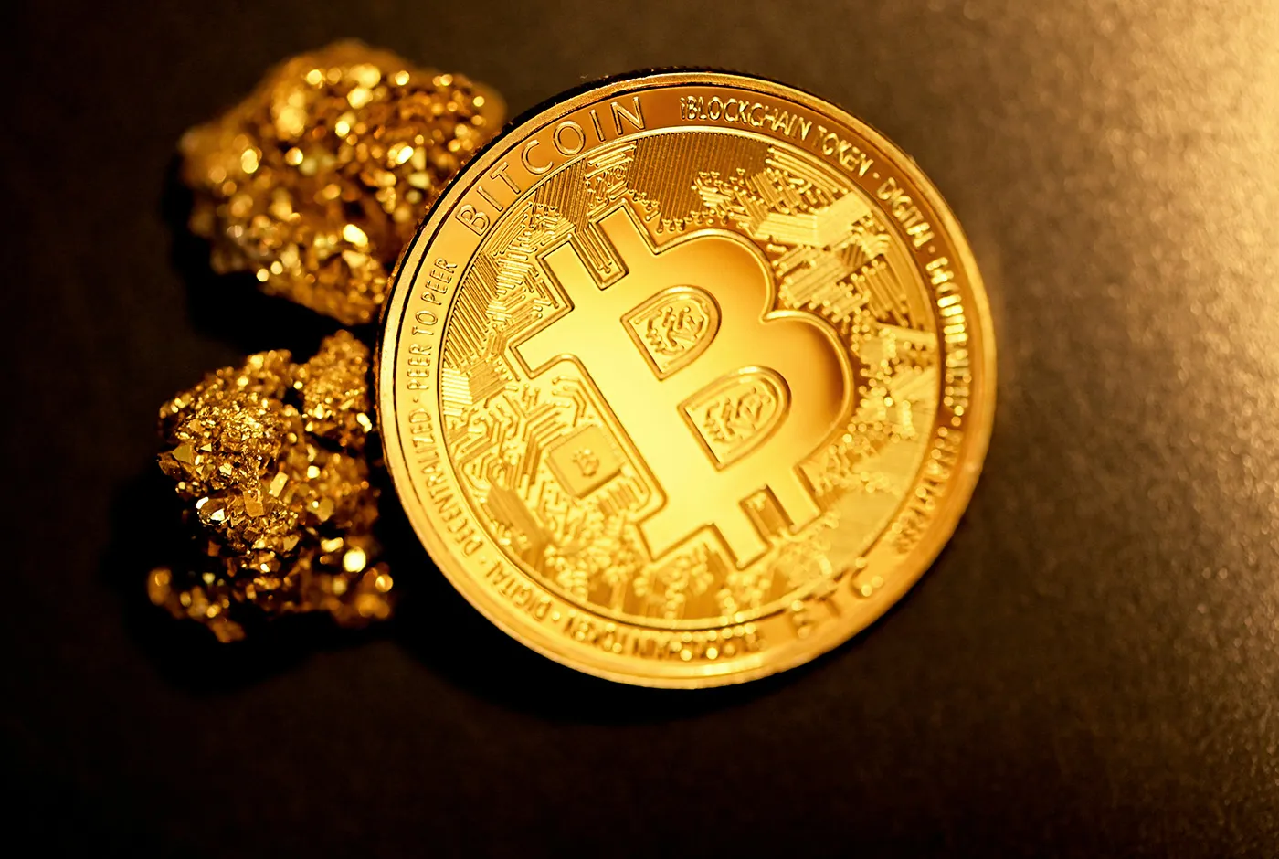 Goldene Bitcoin-Münze neben Goldnuggets auf dunklem Untergrund