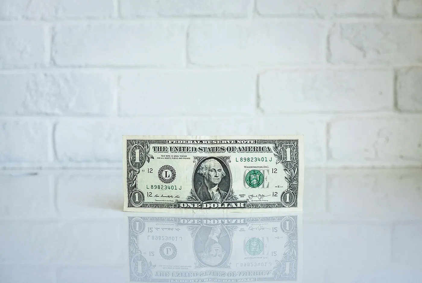 Eine Ein-Dollar-Note steht vor einer weißen Backsteinwand
